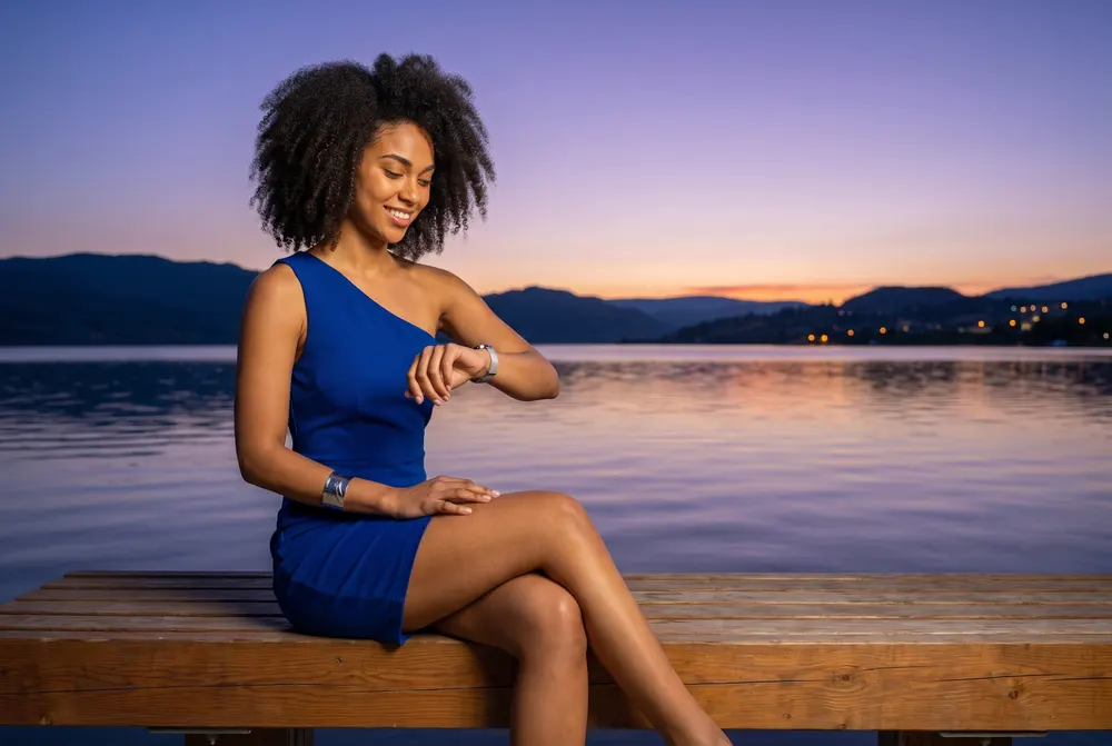 Woman on a lakeside bench at dusk checking her watch